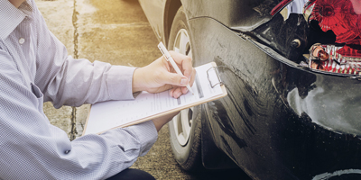 Man writing on clipboard next to damaged car