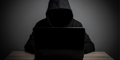 Person in black hoodie behind computer sc