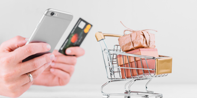 Hand holding phone and credit card with mini trolley next to them