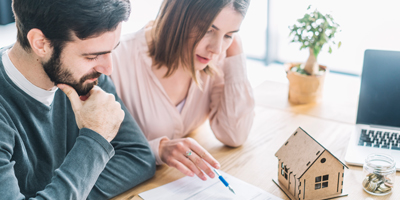 Couple filling out document looking puzzled with model house