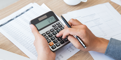 Hands on calculator and holding pen with documents in background