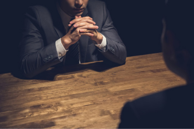 Man with hands clasped sitting at table looking at another man